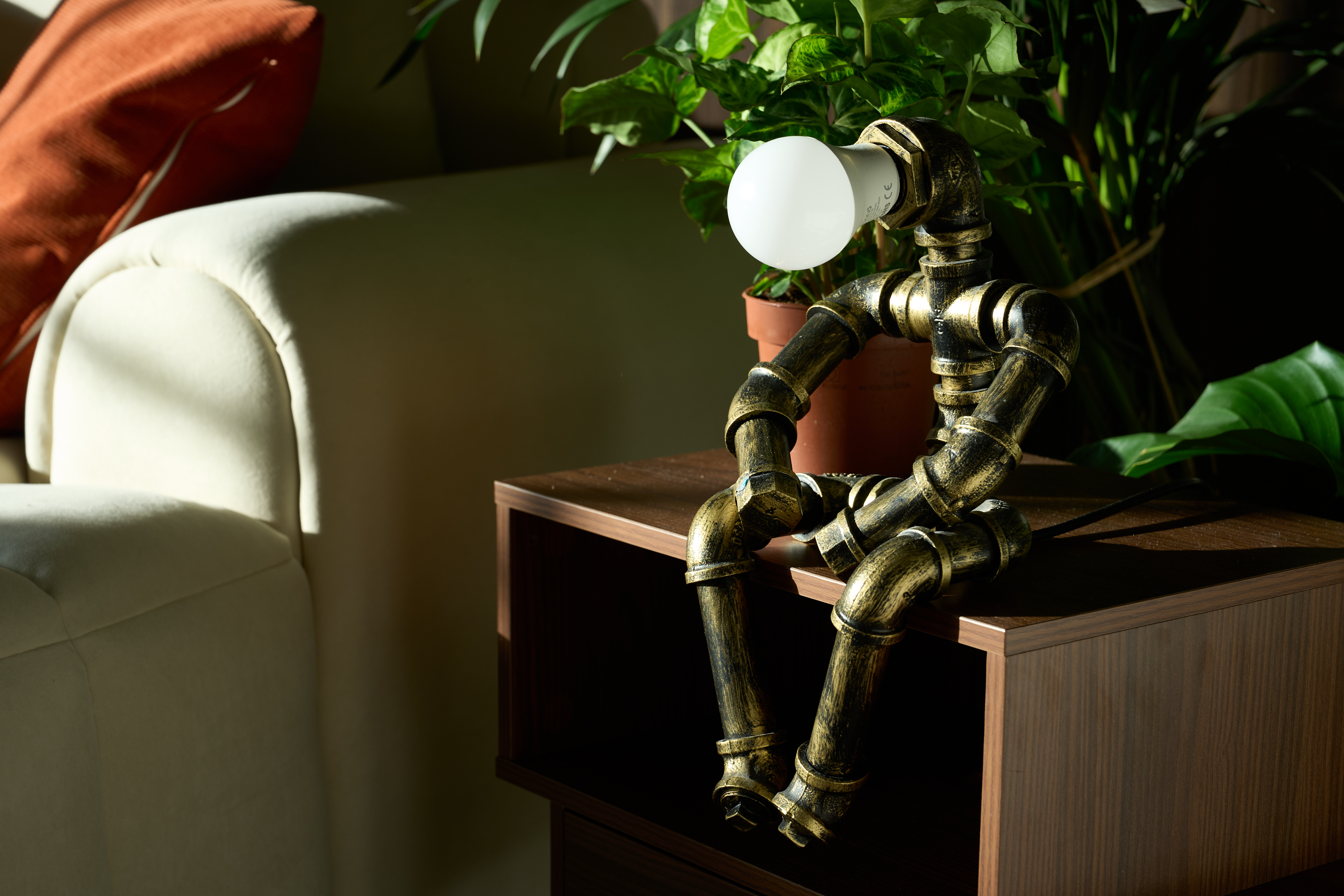Sculptural pipe-figure brass table lamp posed on a walnut sideboard beside the cream sofa at The Designer's Penthouse, Old Street London