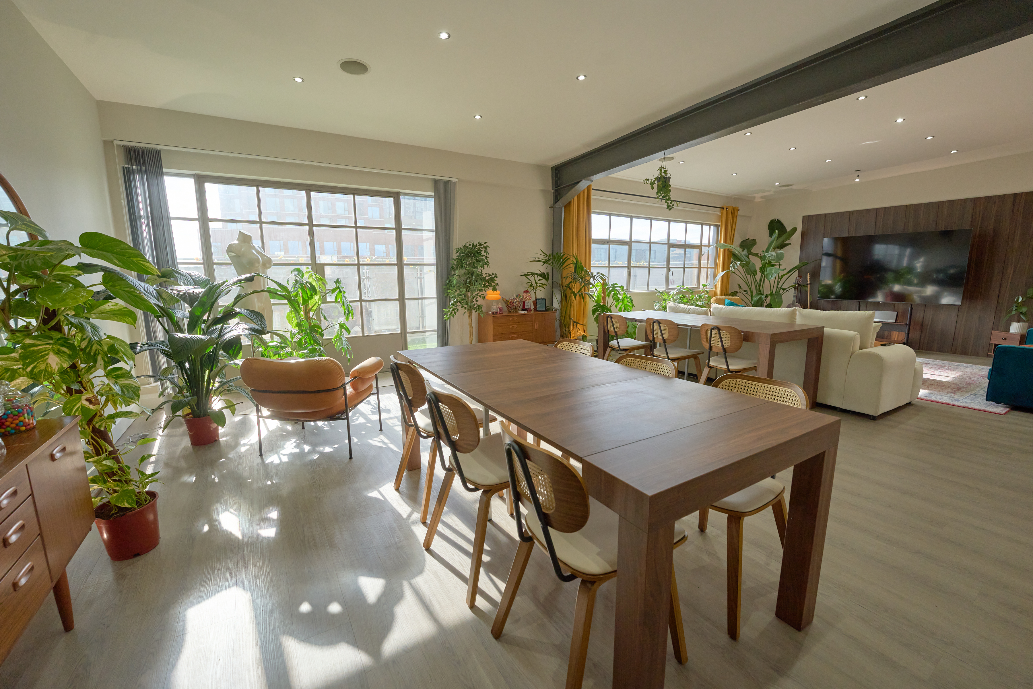 Open-plan dining and lounge area with long walnut table, cane chairs, and industrial steel beam under daylight at The Designer's Penthouse, Old Street London