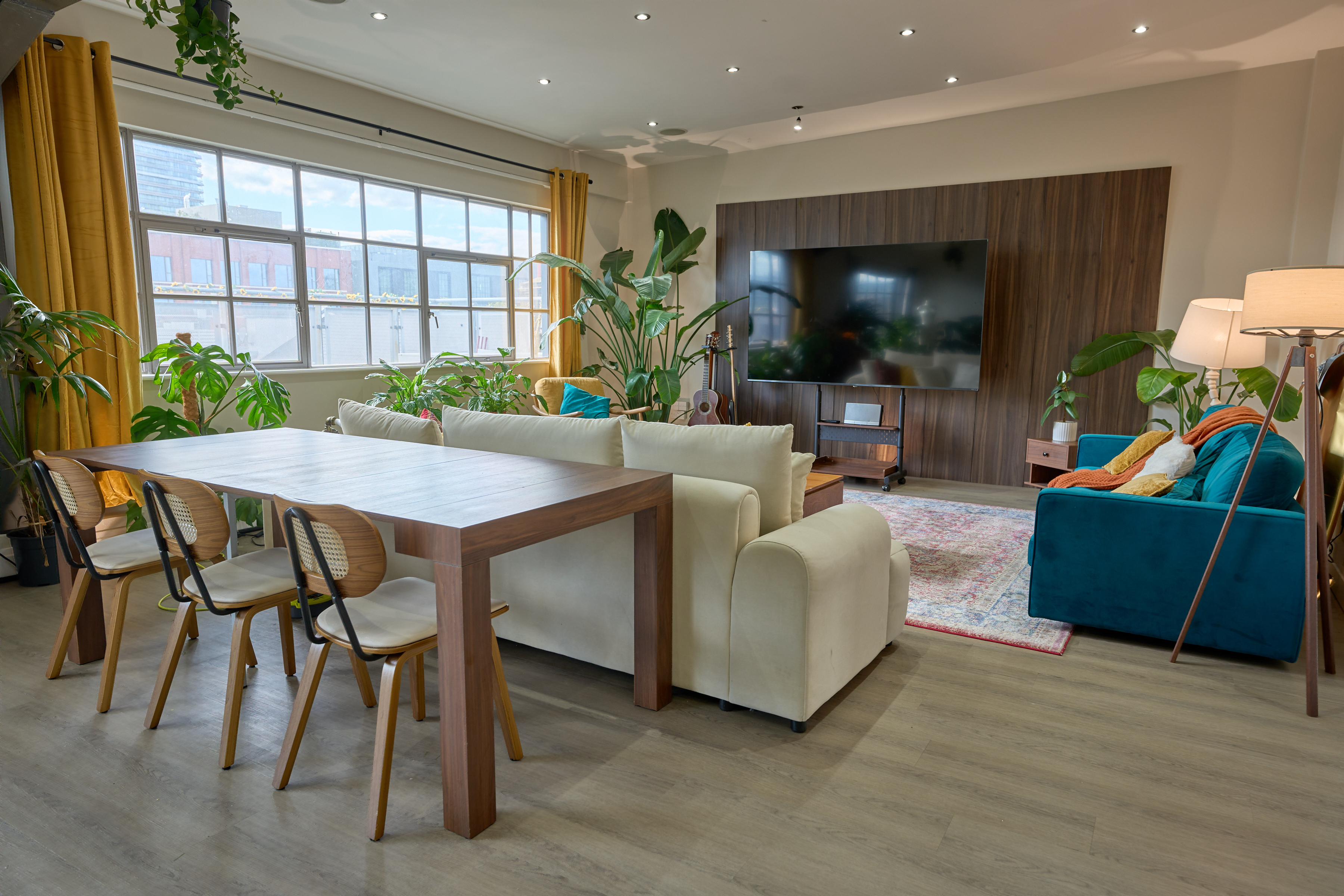 Walnut dining table and cane chairs beside cream lounge seating and media wall at The Designer's Penthouse, Old Street London