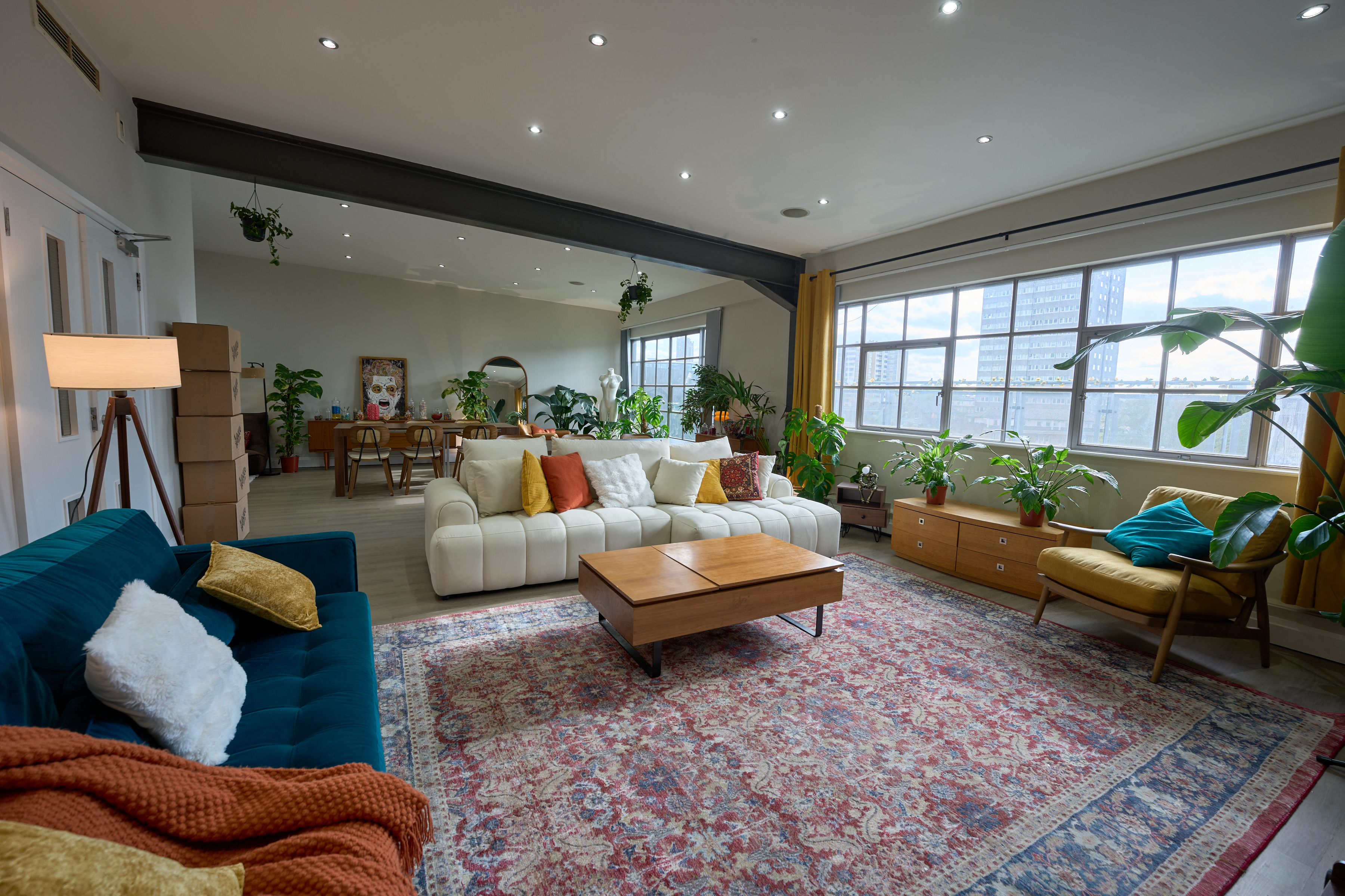 Wide-angle view of the open-plan lounge with teal velvet sofa, Persian rug, and London skyline windows at The Designer's Penthouse, Old Street
