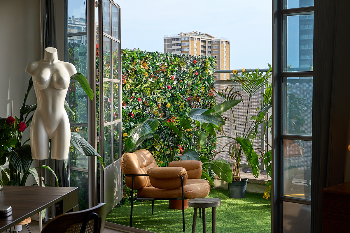 Open french doors framed by a sculptural mannequin and plants revealing the rooftop flower wall and summer terrace at The Designer's Penthouse, Old Street London