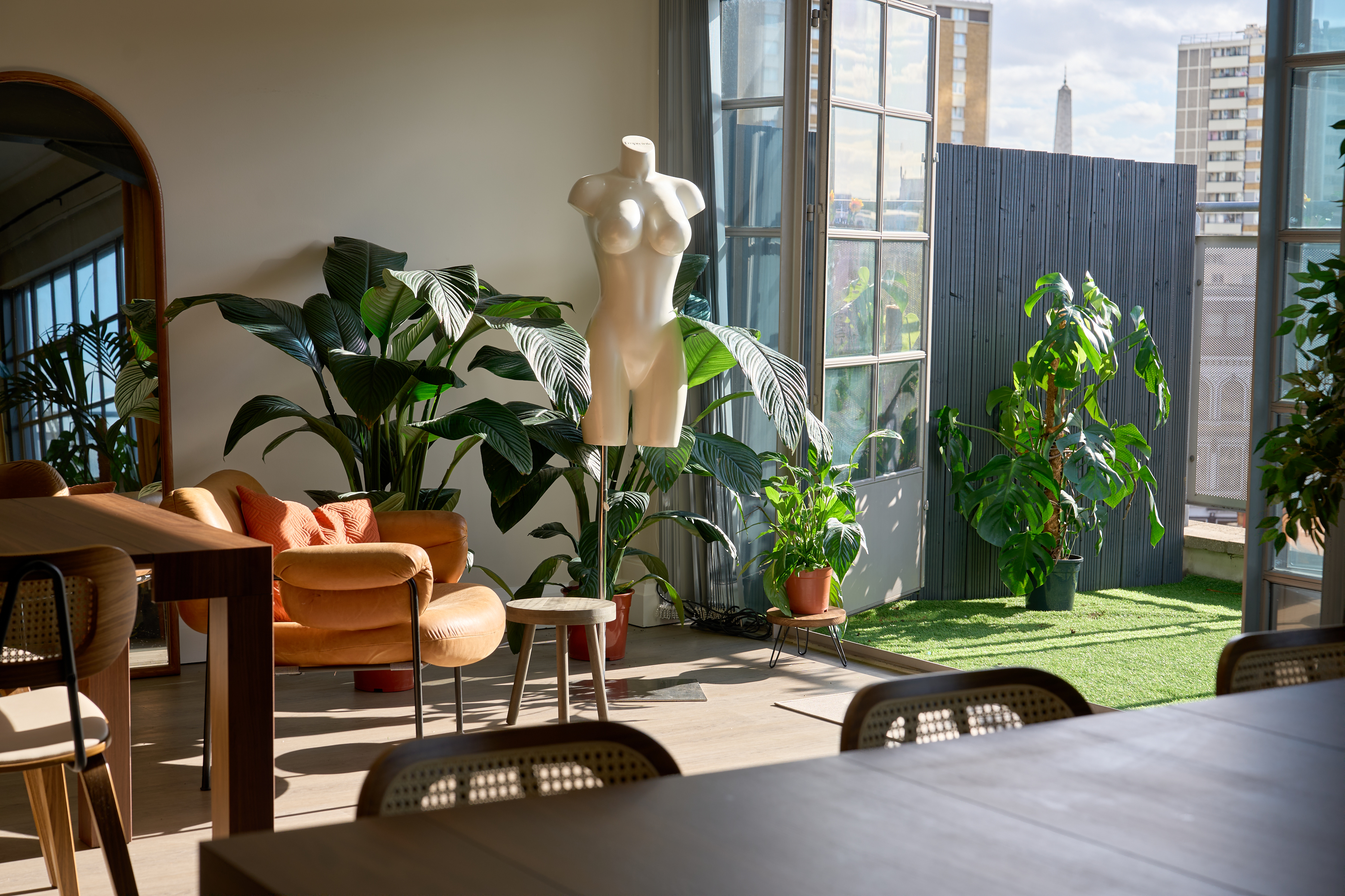 Artist mannequin and lush plants beside open doors onto the rooftop terrace with London skyline view at The Designer's Penthouse, Old Street