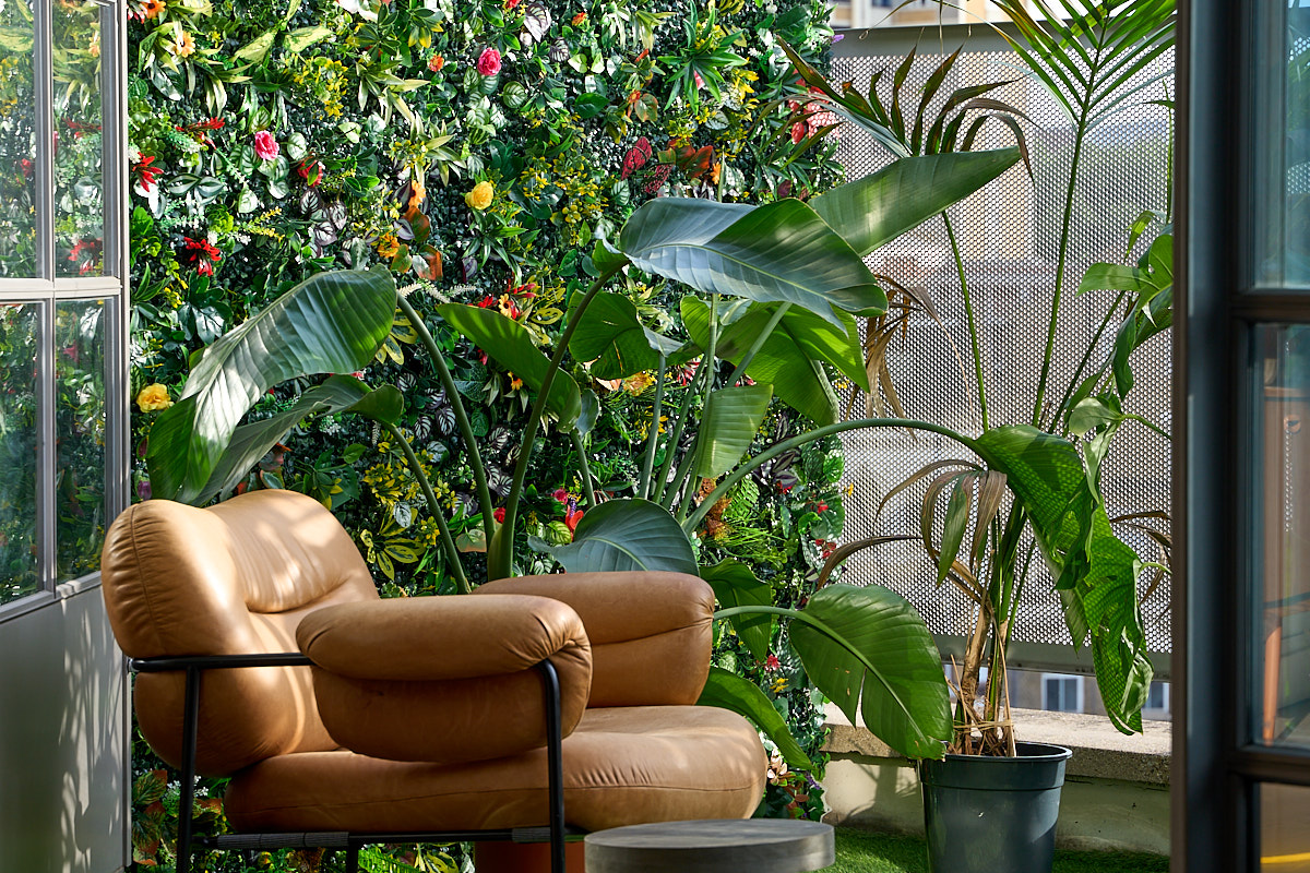 Tan leather armchair beside a blooming flower wall and palm foliage in dappled summer light on the terrace at The Designer's Penthouse, Shoreditch
