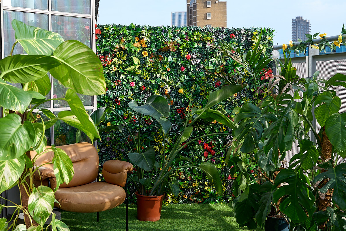 Rooftop terrace with a full artificial flower wall, tan leather armchair, and layered greenery under summer daylight at The Designer's Penthouse, Old Street London